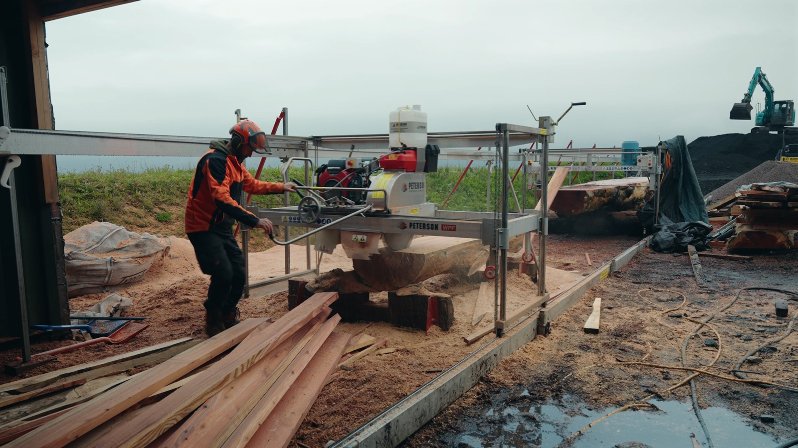 An operator sawing an opened log, with sawn pieces alongside the mill